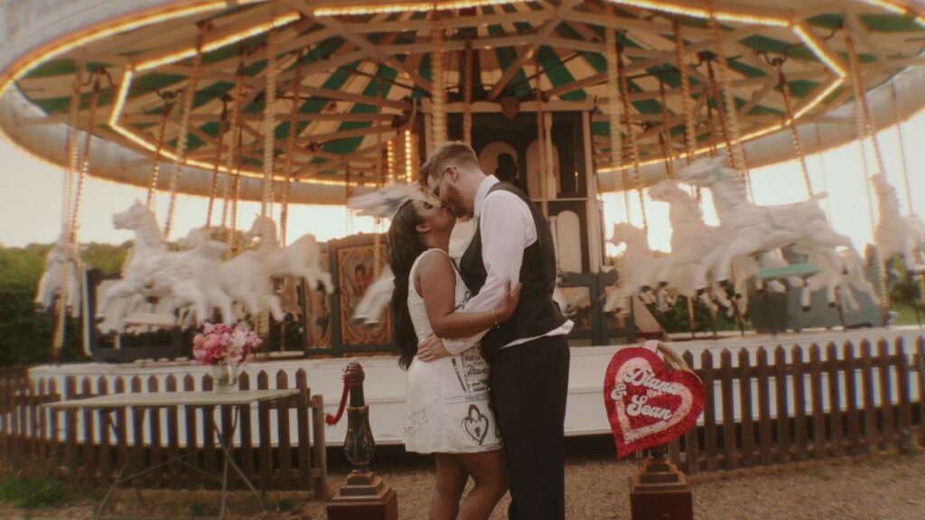 A couple share a kiss by a fun fair carousel at Preston Court Wedding Venue. This was captured on their wedding day by Wedding Videographer HC Visuals 